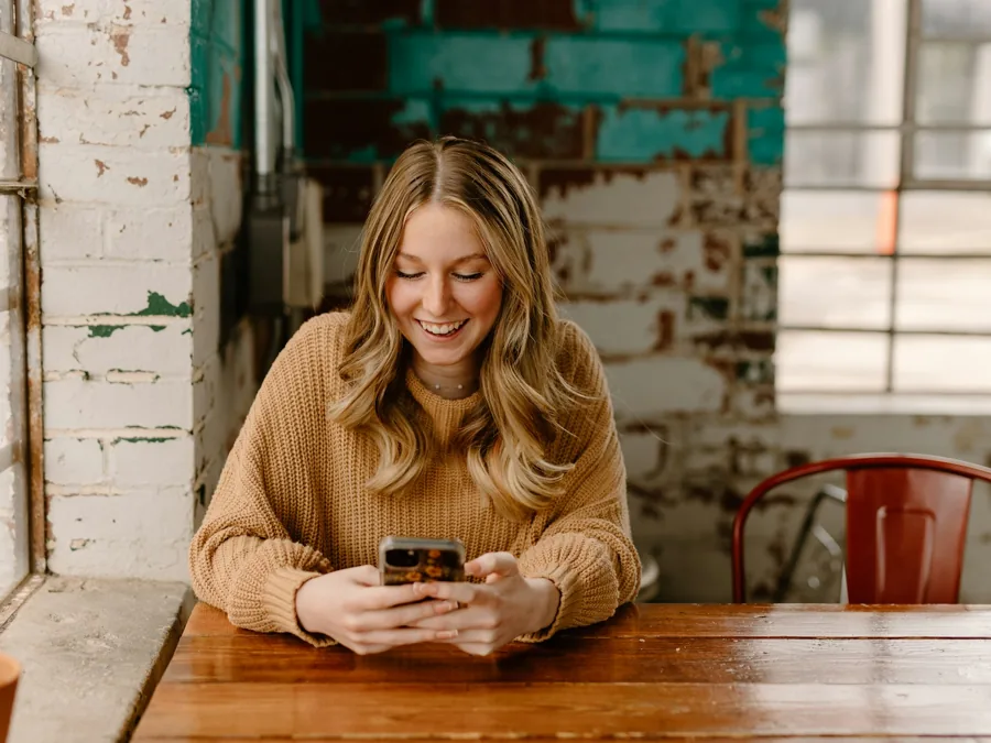 A woman at her kitchen table reading a message on her phone